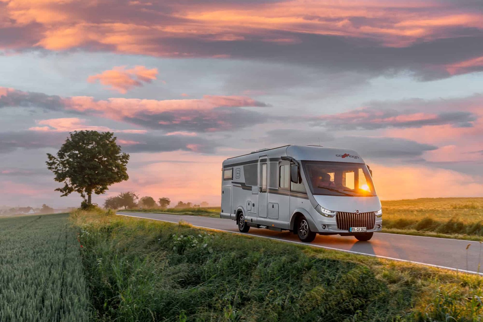 An RV is driving down a country road at sunset, showcasing the class and elegance of this recreational vehicle.