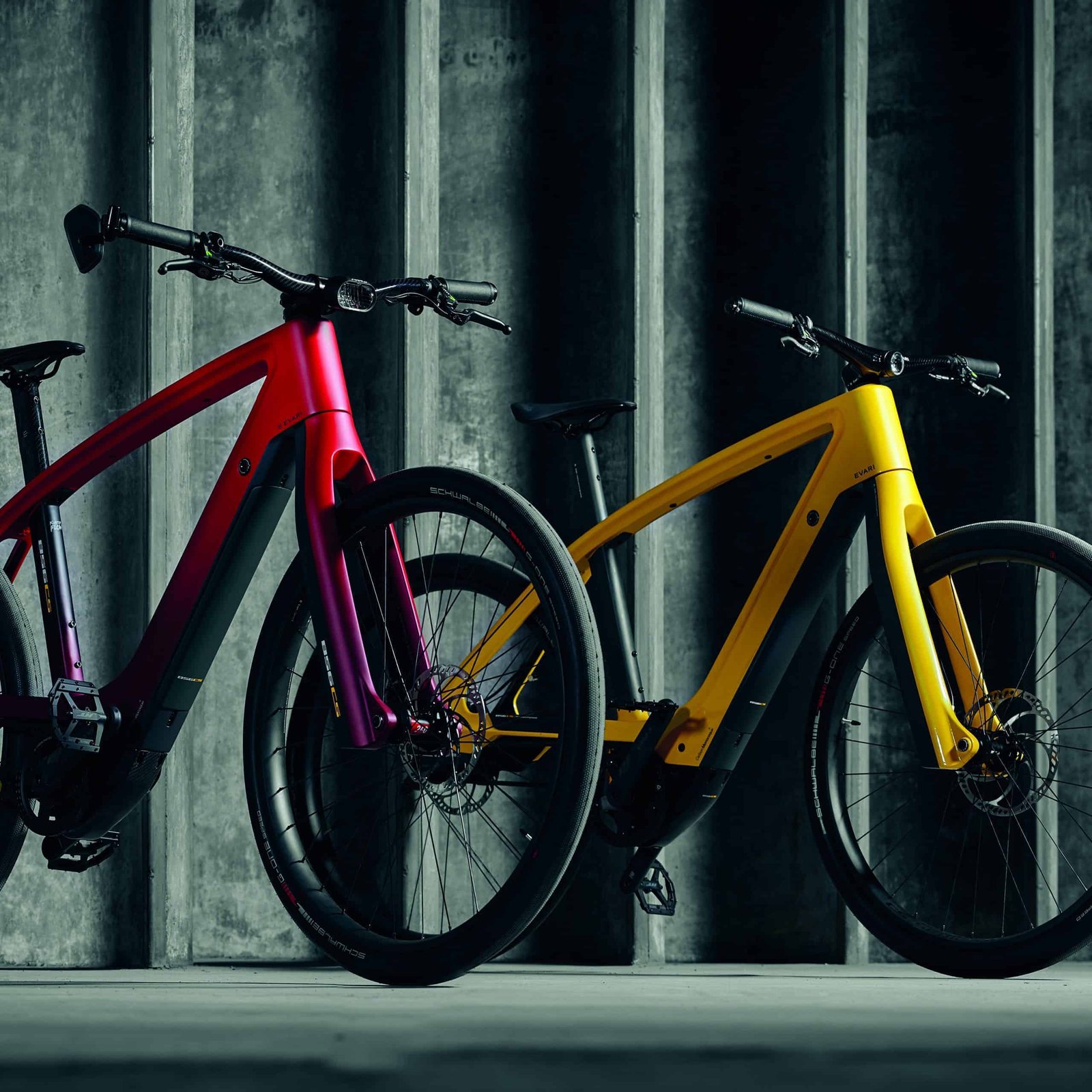 Two electric bikes with vibrant colors are parked in front of a concrete wall.