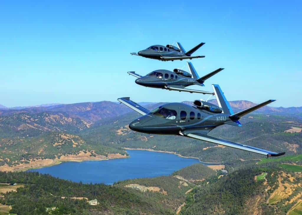 Three small planes jetting over a lake.