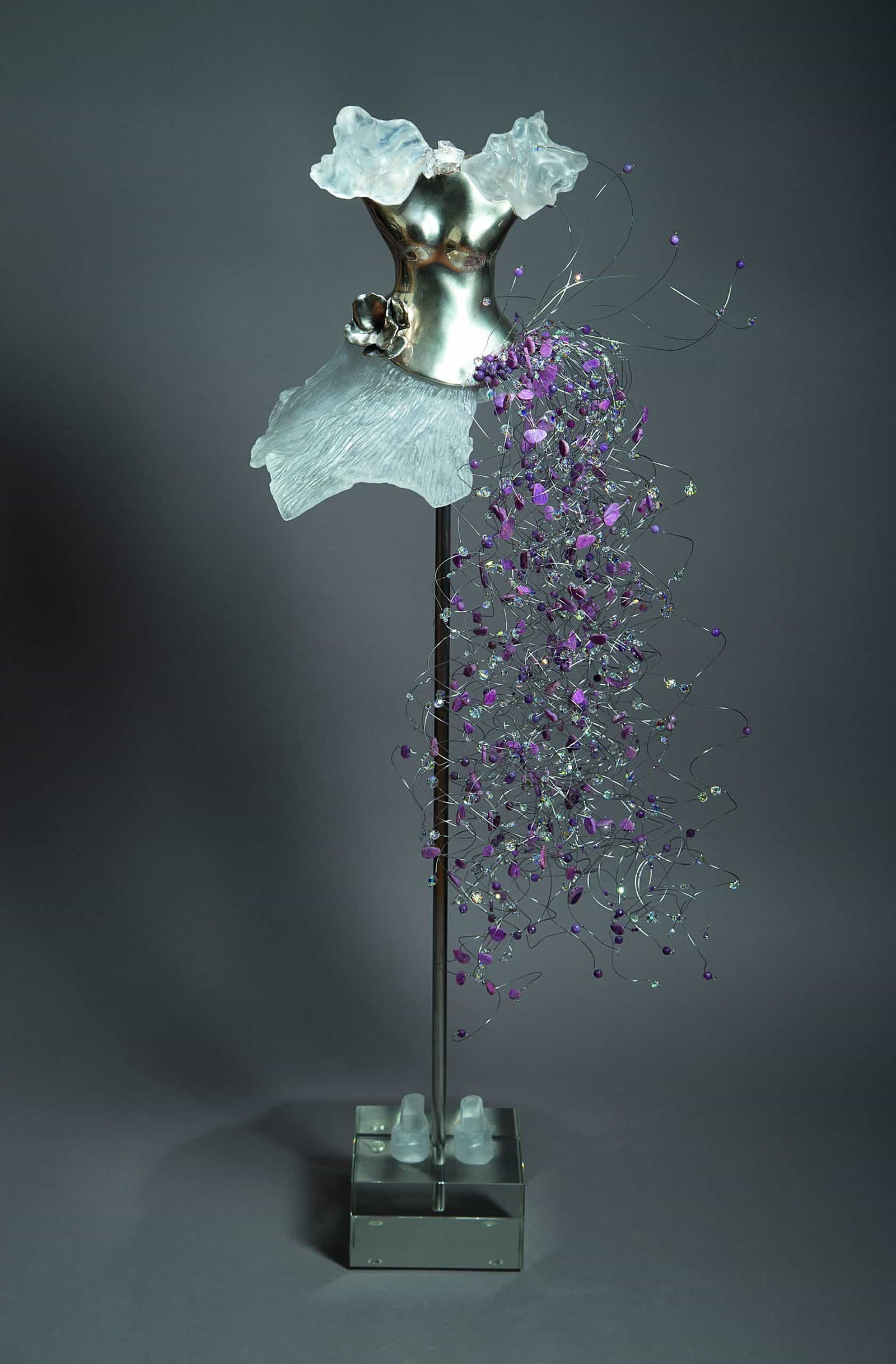 A silver sculpture with a feminine touch on a stand, featuring hints of purple.