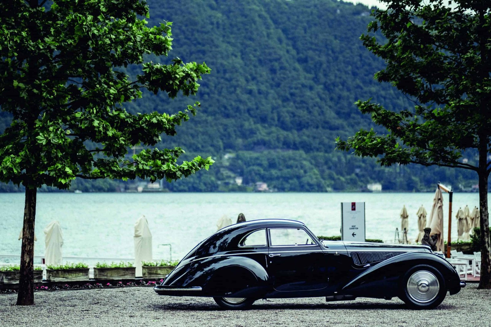 A wind-shaped black car parked by the lake.