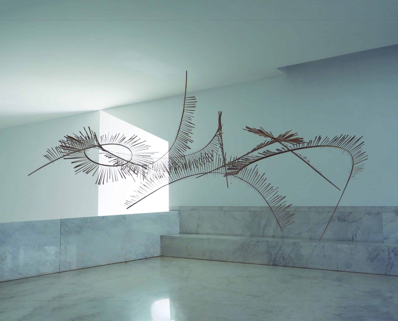 A white room with a sculpture on the wall, illuminated by soft light.