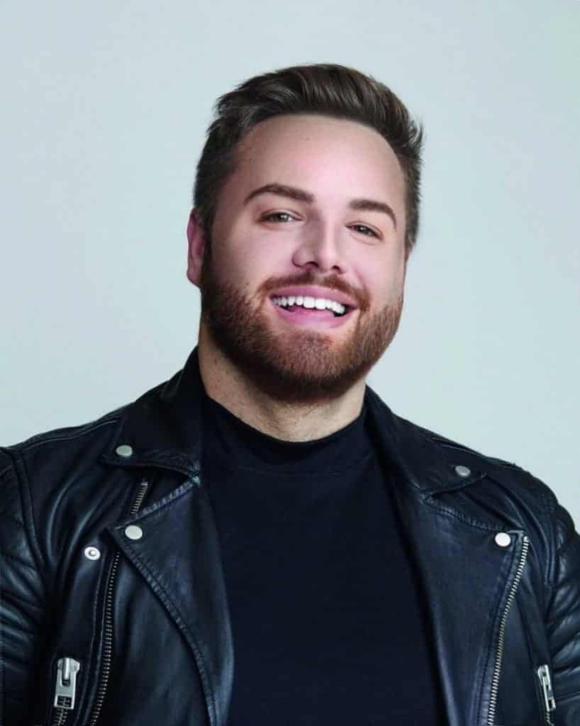 A man in a black leather jacket exudes alluring beauty as he smiles.