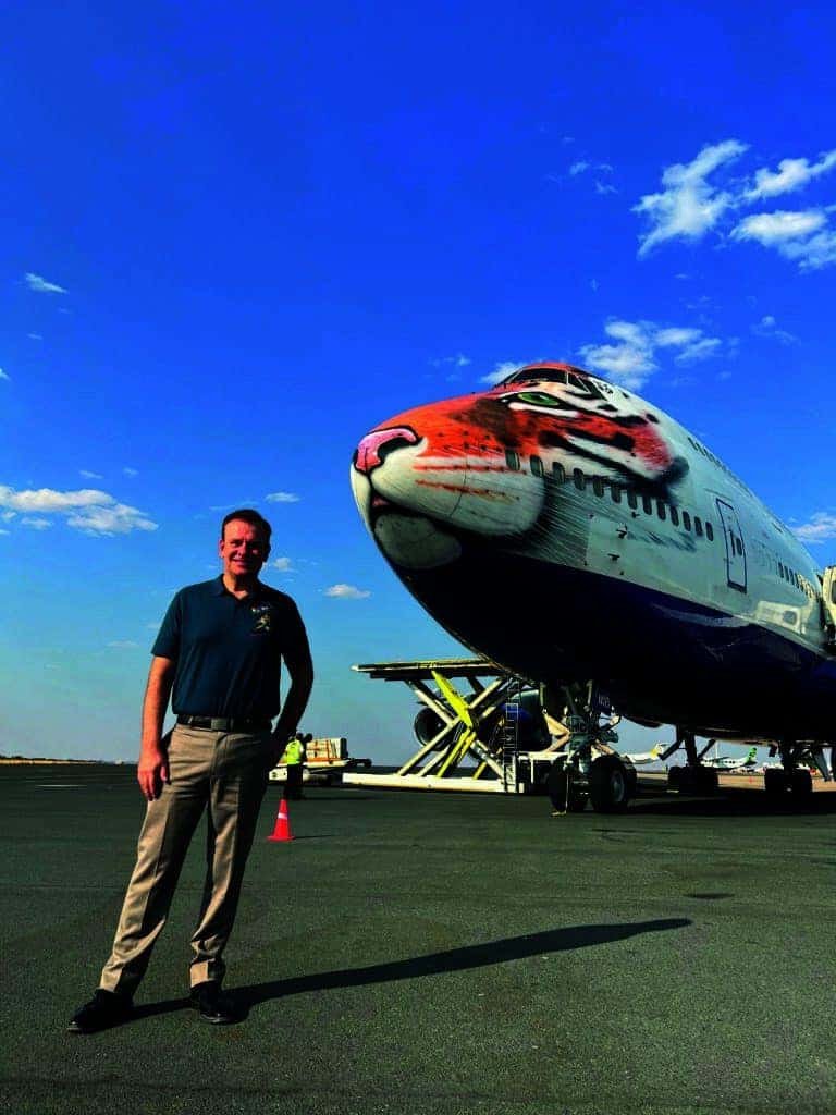 A pioneer in aviation stands next to an airplane with a tiger on it.