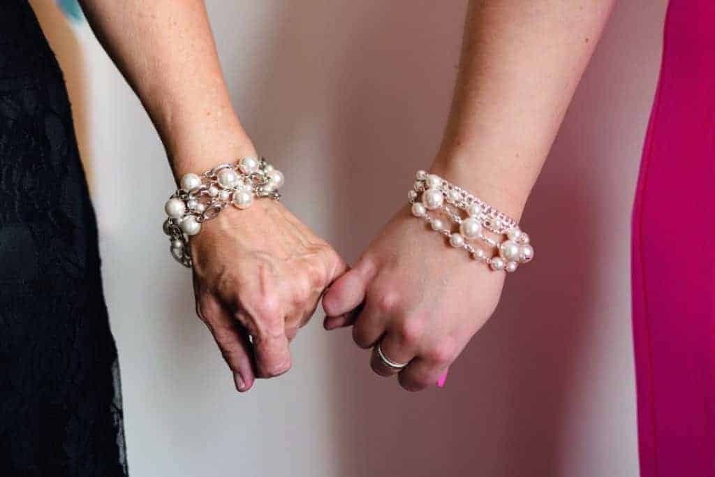Two women holding hands, both wearing statement-making pearl bracelets.