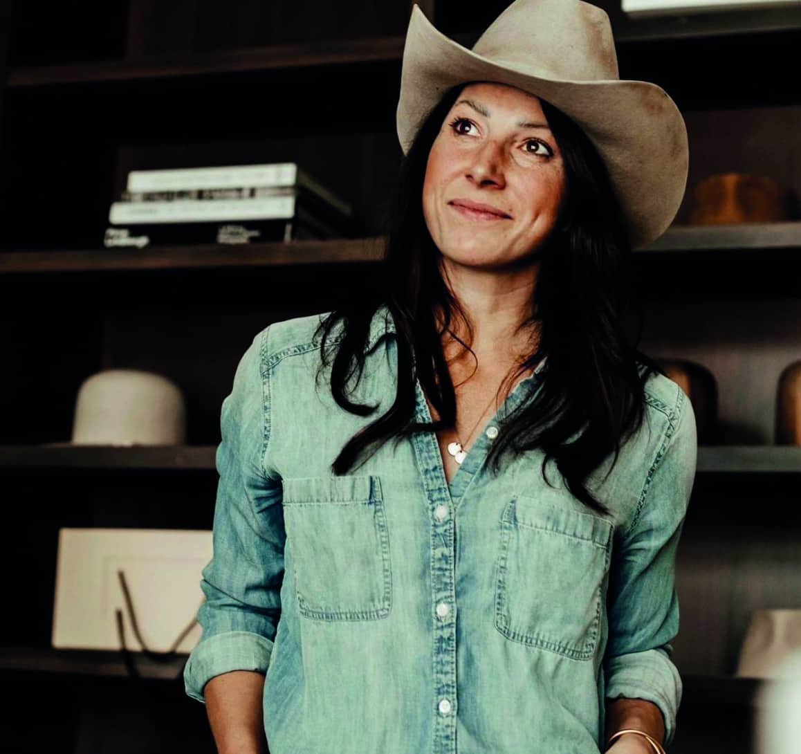 A woman in a cowboy hat standing in front of a shelf in a western story setting.