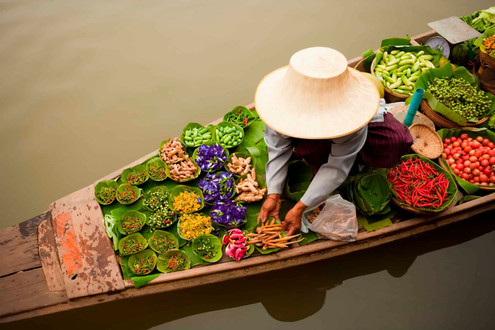 A woman in a hat is selling vegetables on a boat while traveling.