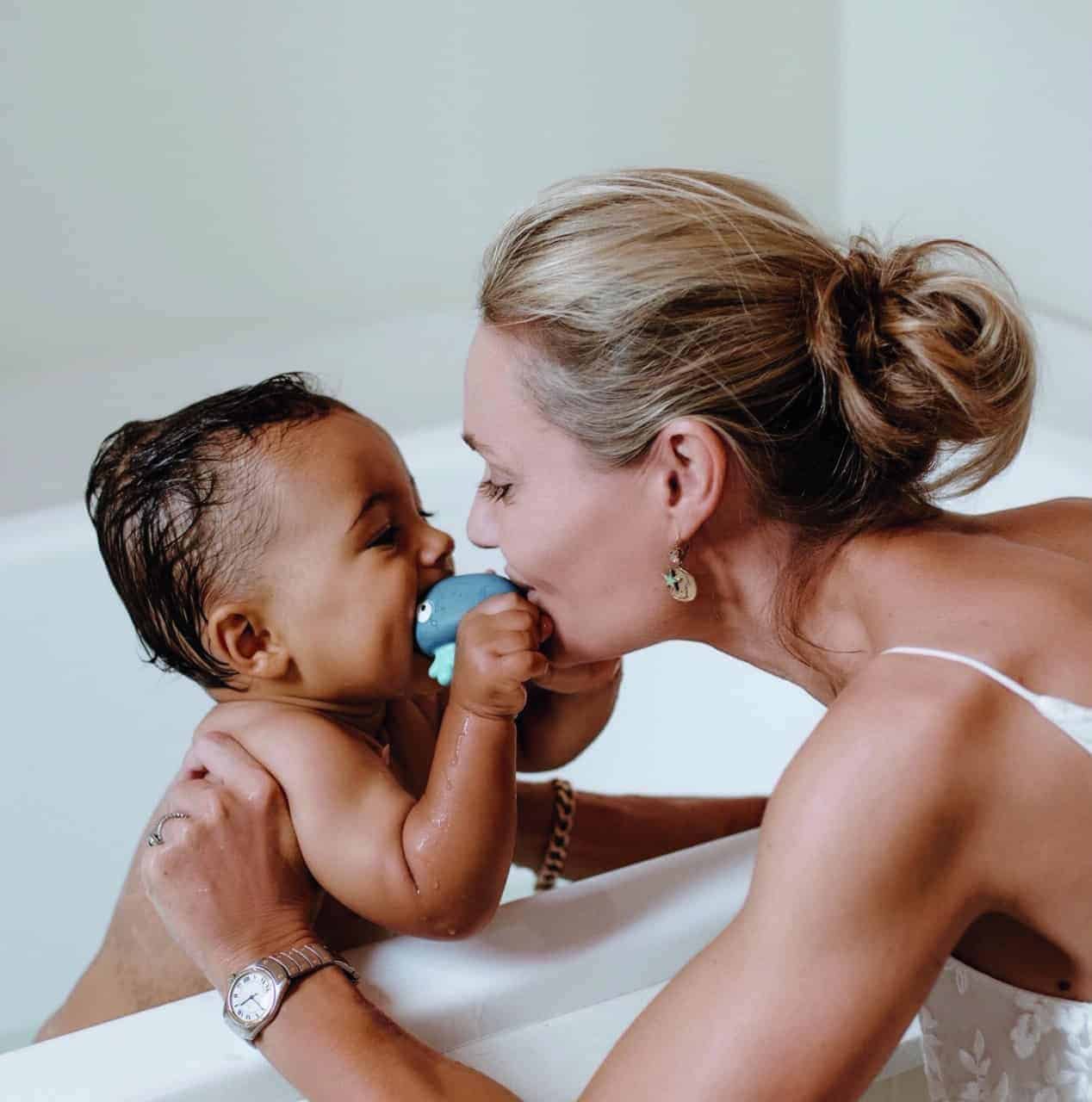 A woman carefully brushes her baby's teeth in a bathtub, ensuring every tooth is clean and healthy.