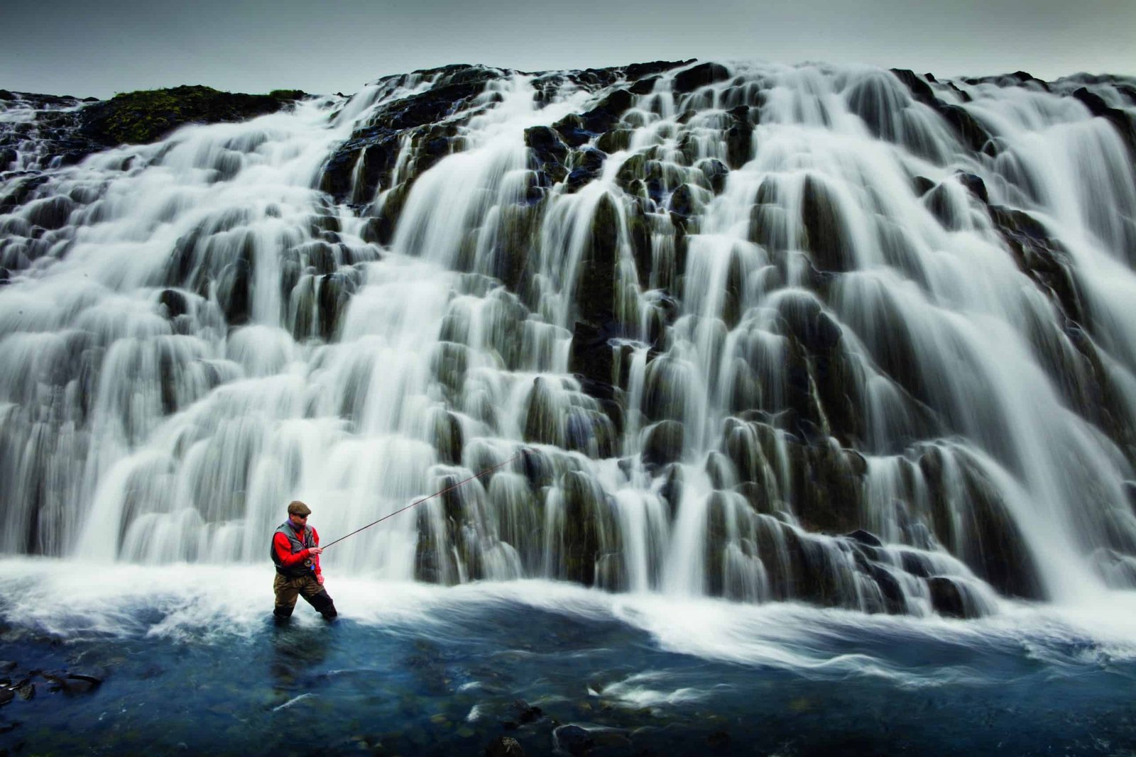 A man is standing in front of a **waterfall** during one of his **trips**.