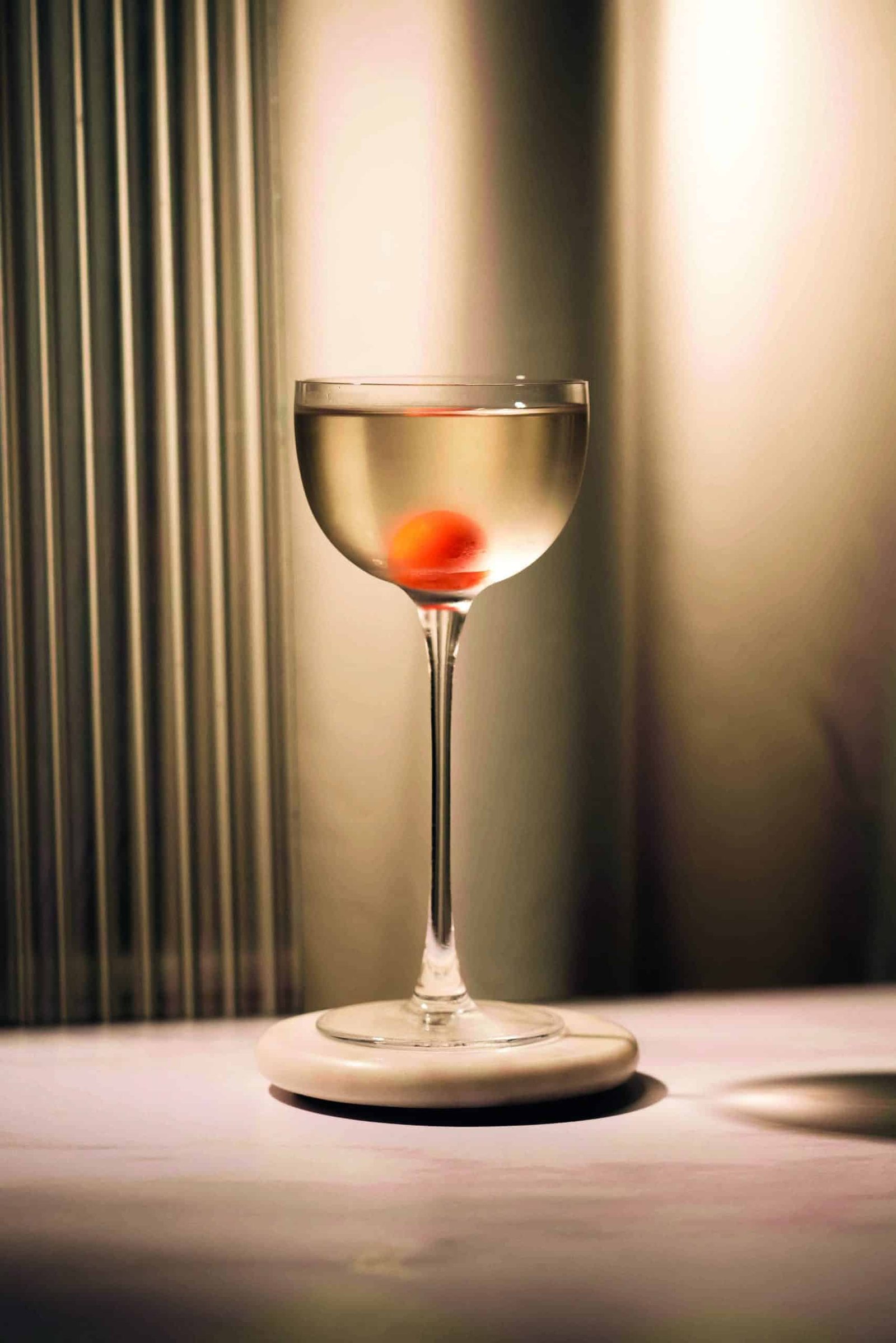 A martini glass with a spirited red cherry in it.