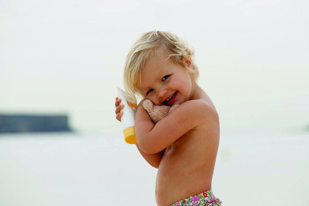 A little girl holding a teddy bear on the beach, enjoying the warm sand and gentle lapping of waves.