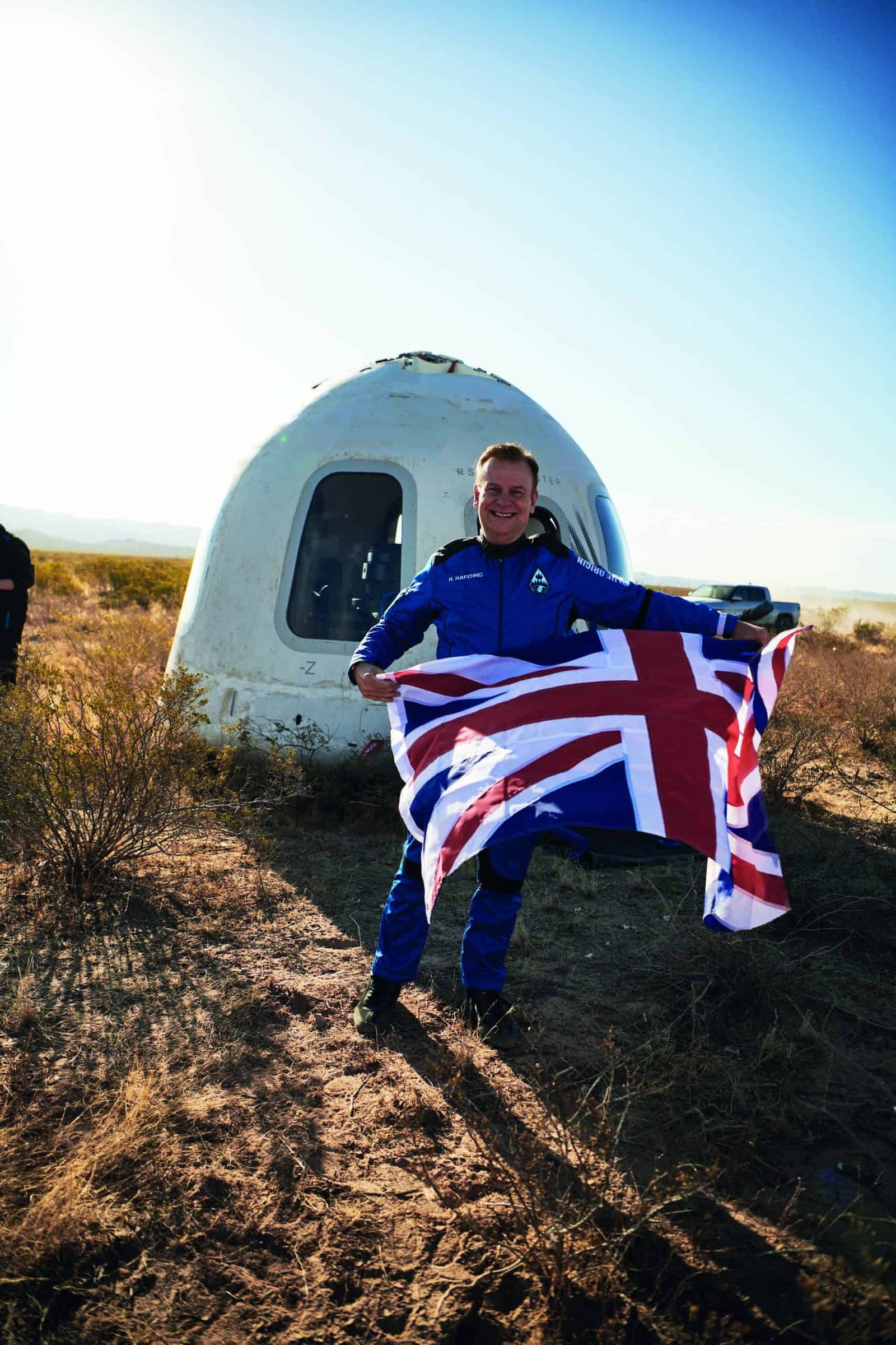 A pioneer holding a British flag in front of a spacecraft.
