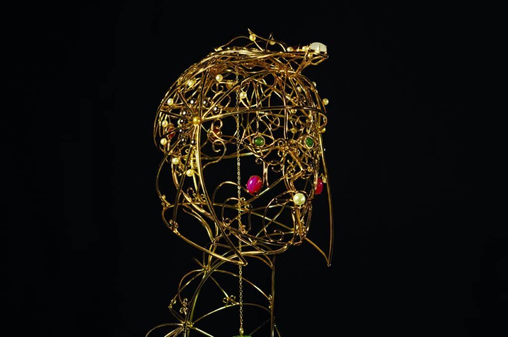 A bejeweled gold wire sculpture of a woman's head on a black background, beautifully balancing form and delicacy.