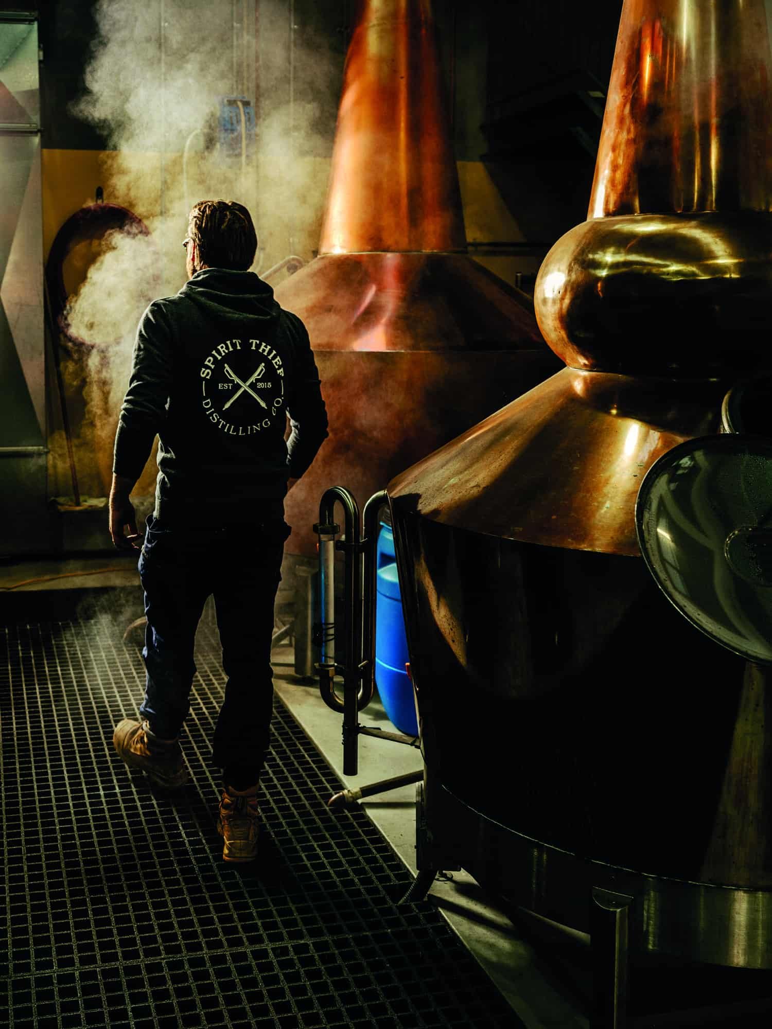 A man in a hoodie walking through a grape distillery.
