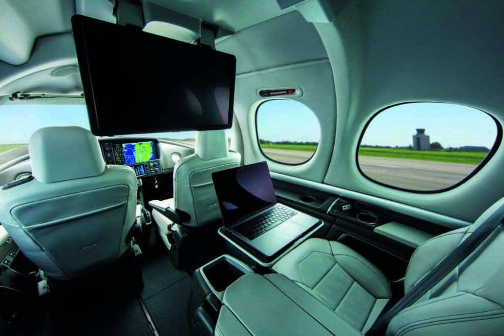The future of Jetting is showcased within the interior of a plane, where a laptop and a monitor are prominently featured.