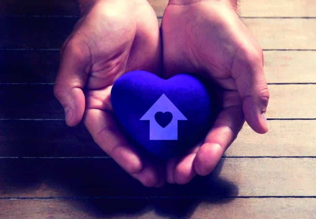 Two hands turning dreams into reality, holding a blue heart with a house on it.