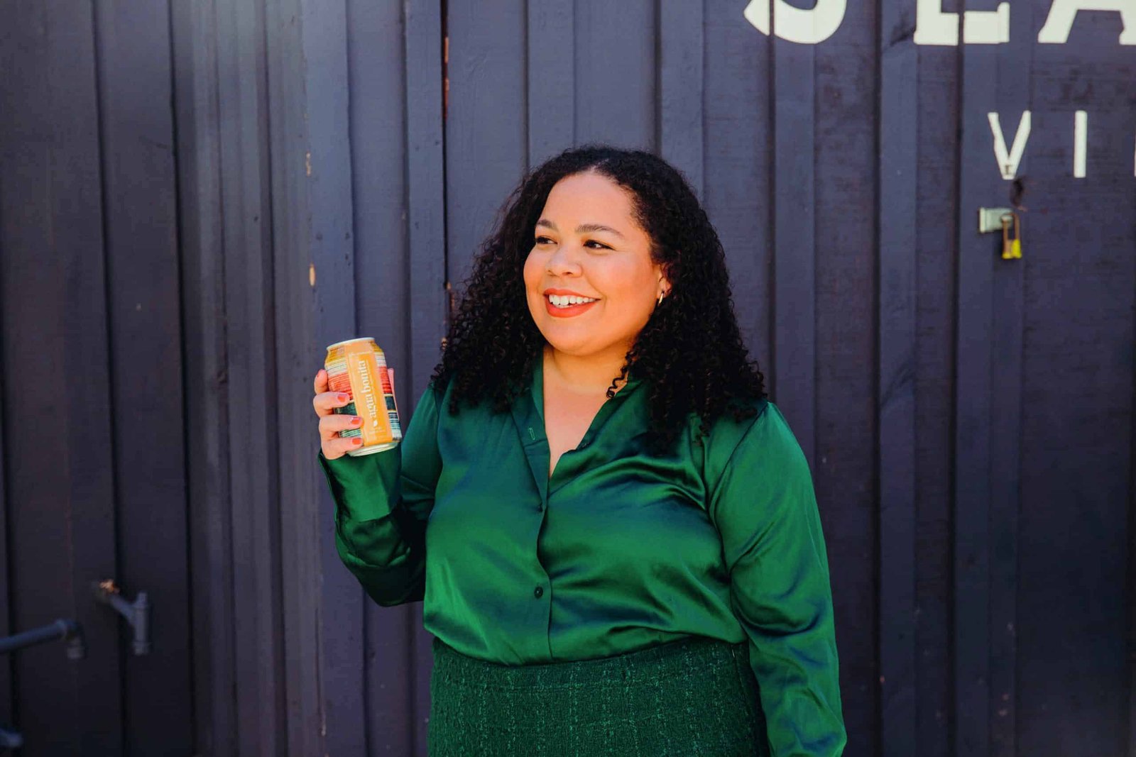 A Latin woman in a green shirt and green skirt holding a beer.
